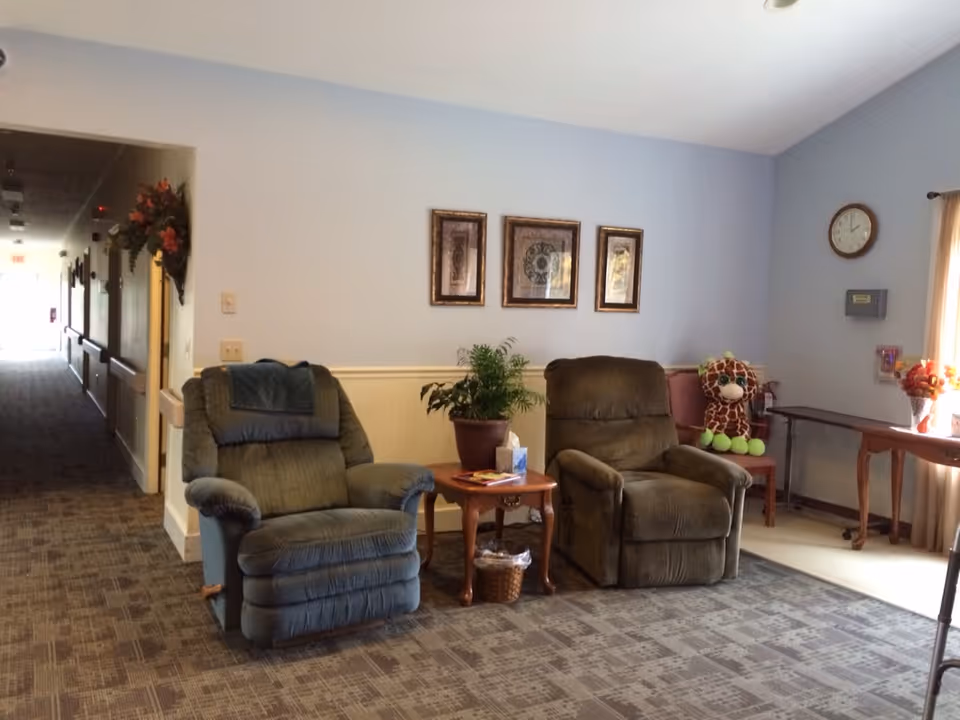 Two recliner chairs with side table, plant, and a giraffe plush in a living room.