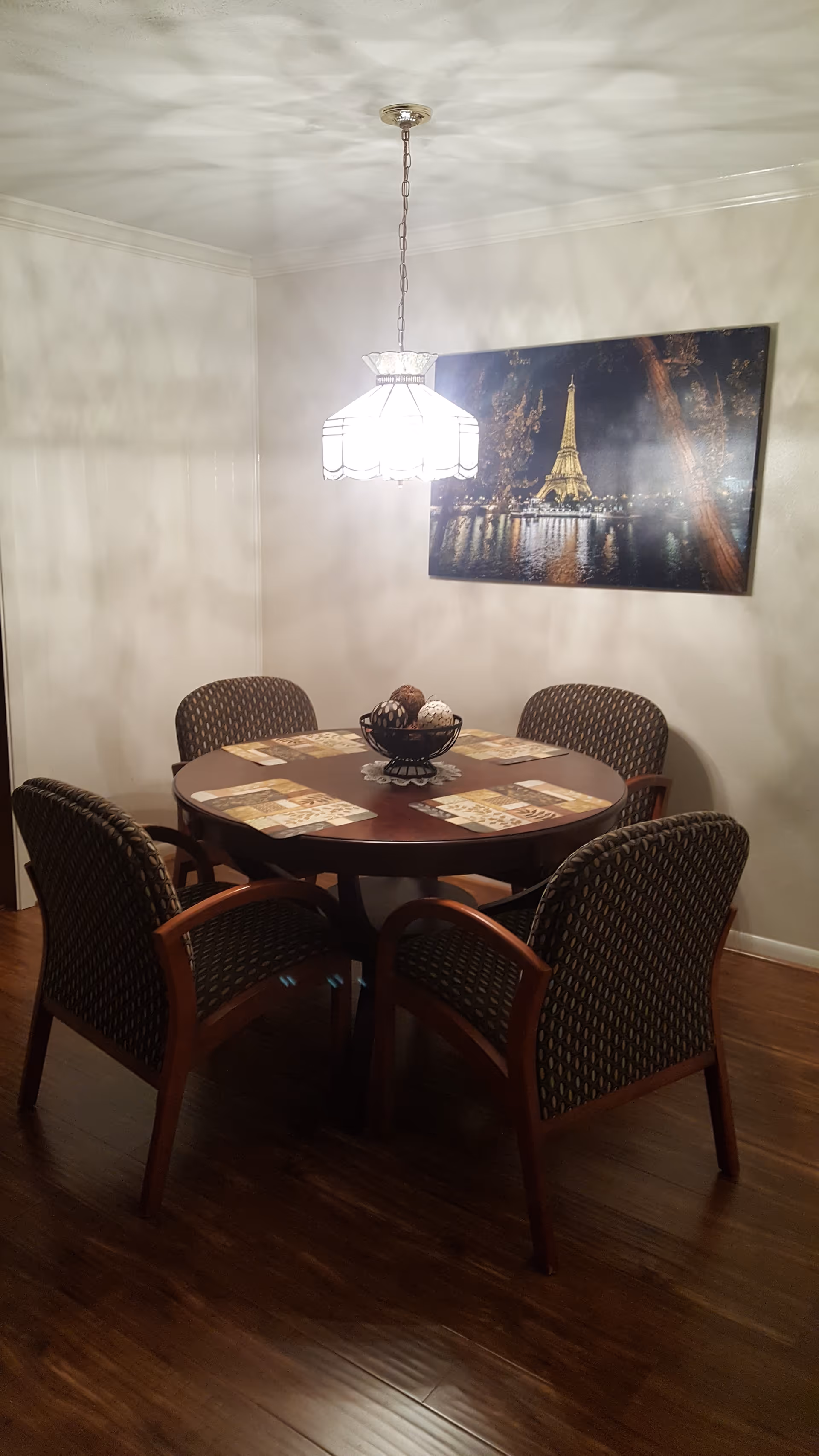 Round wooden dining table with chairs under a hanging light in a dining room.