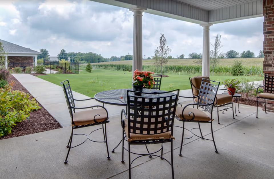 A patio area with metal chairs and a table overlooking a grassy field.