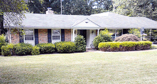 Single-story brick senior living facility with a covered front porch and manicured shrubs.