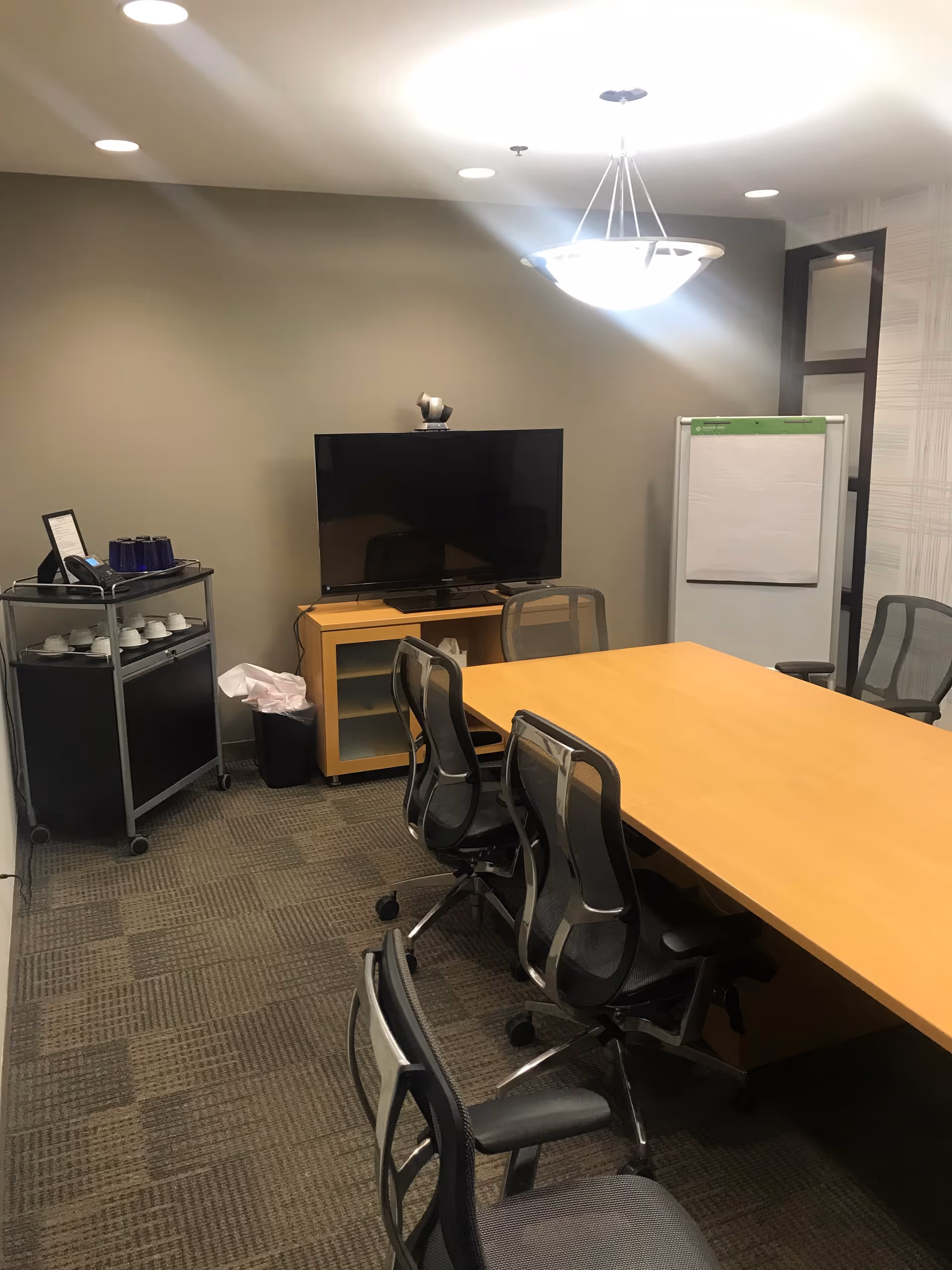 Conference room with long table, chairs, TV, flip chart, and coffee cart.