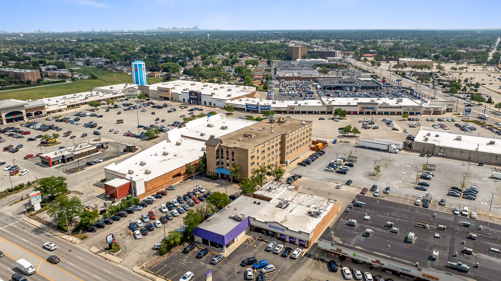 Aerial view of a shopping plaza with parking lots and surrounding commercial buildings.