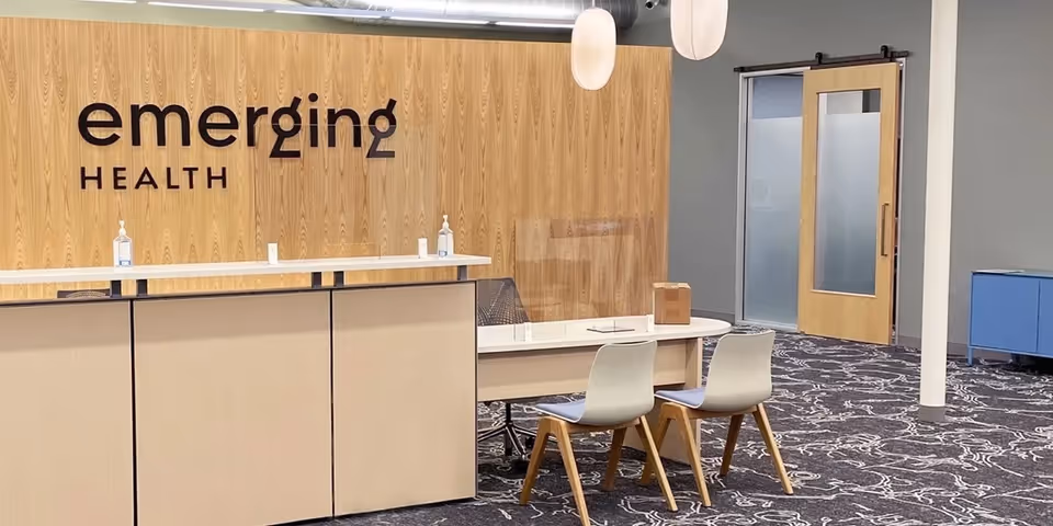 Reception area with wood panel wall, 'Emerging Health' sign, counter, and seating.