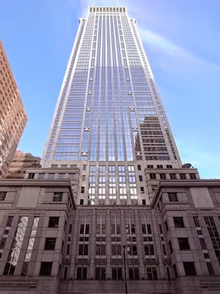 Tall modern skyscraper viewed from street level against a clear blue sky and ornate base.