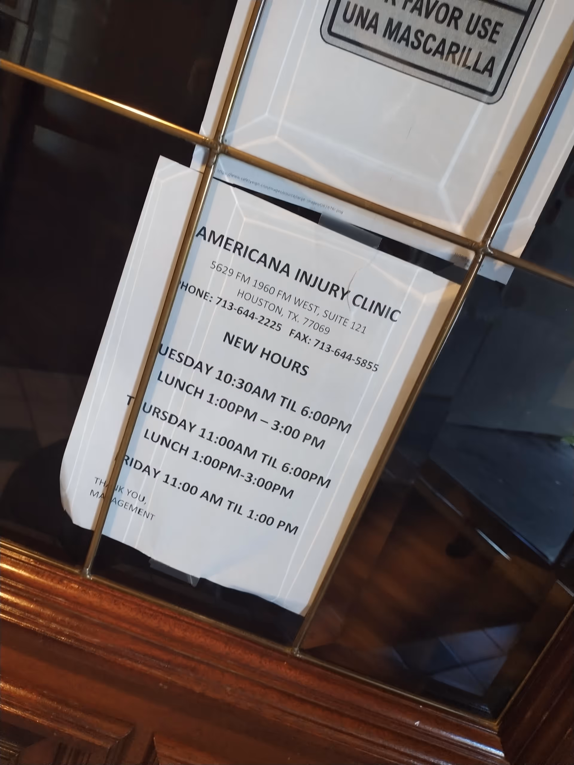 Framed clinic hours notice posted inside a glass door showing hours and contact details.
