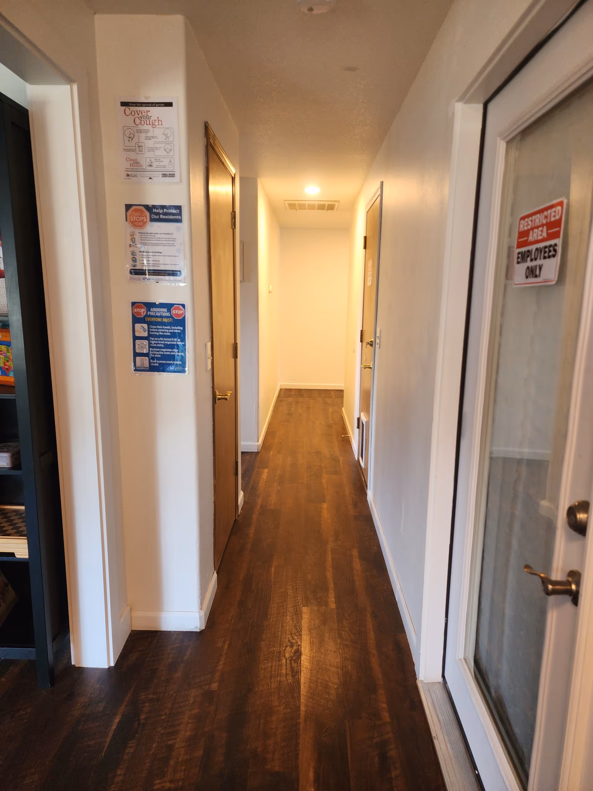 Bright, narrow hallway inside a senior living facility with doors and wall notices.