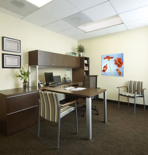 Office area with desk, computers, cabinets, chairs, and wall art in a reception area.