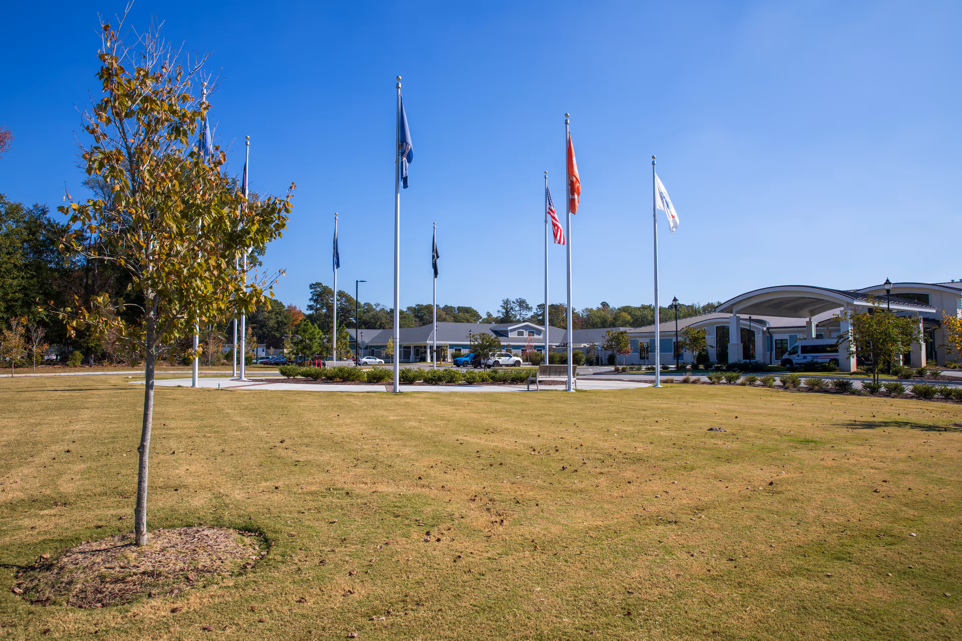 Exterior view of Veteran Village senior living facility with flagpoles and a curved entrance canopy.