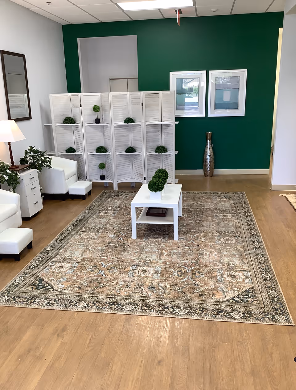 Bright waiting area with white chairs, a rug, and green accent wall.