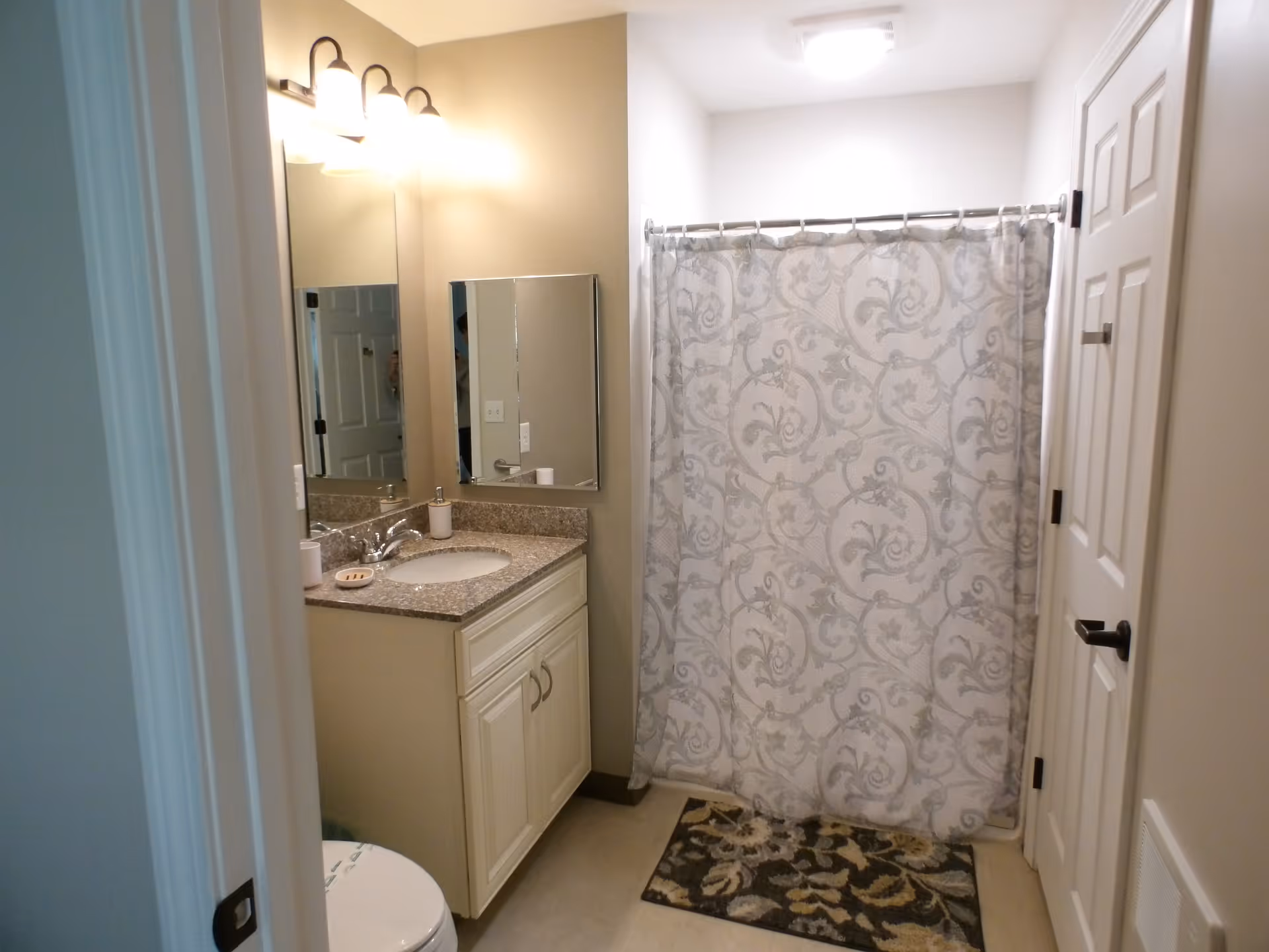 Small bathroom with a sink and vanity under mirrors on the left and a shower with a patterned curtain on the right.