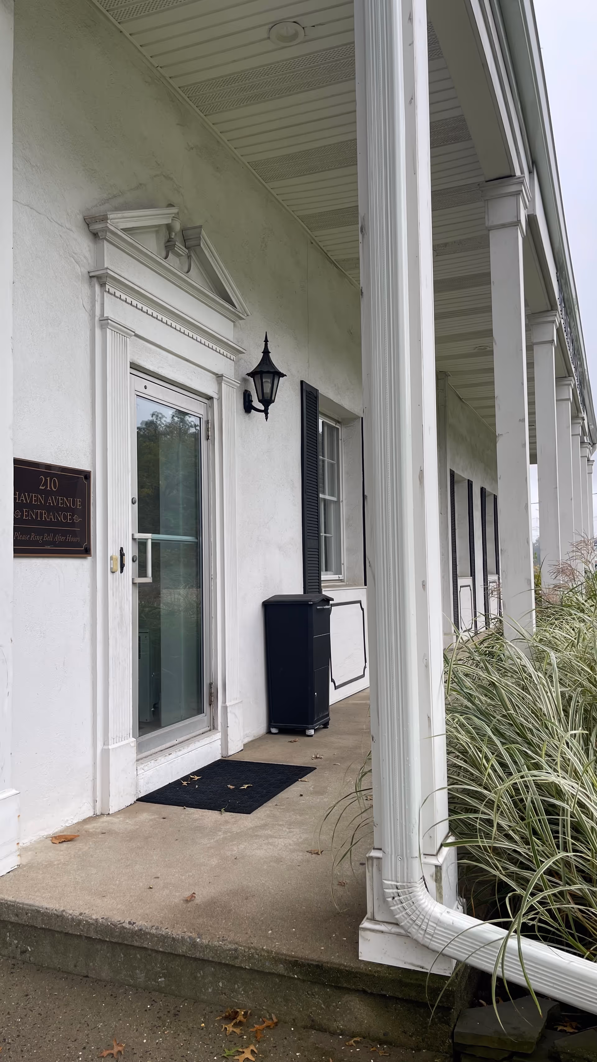 Exterior entrance of a senior living facility with white columns and a black mailbox.