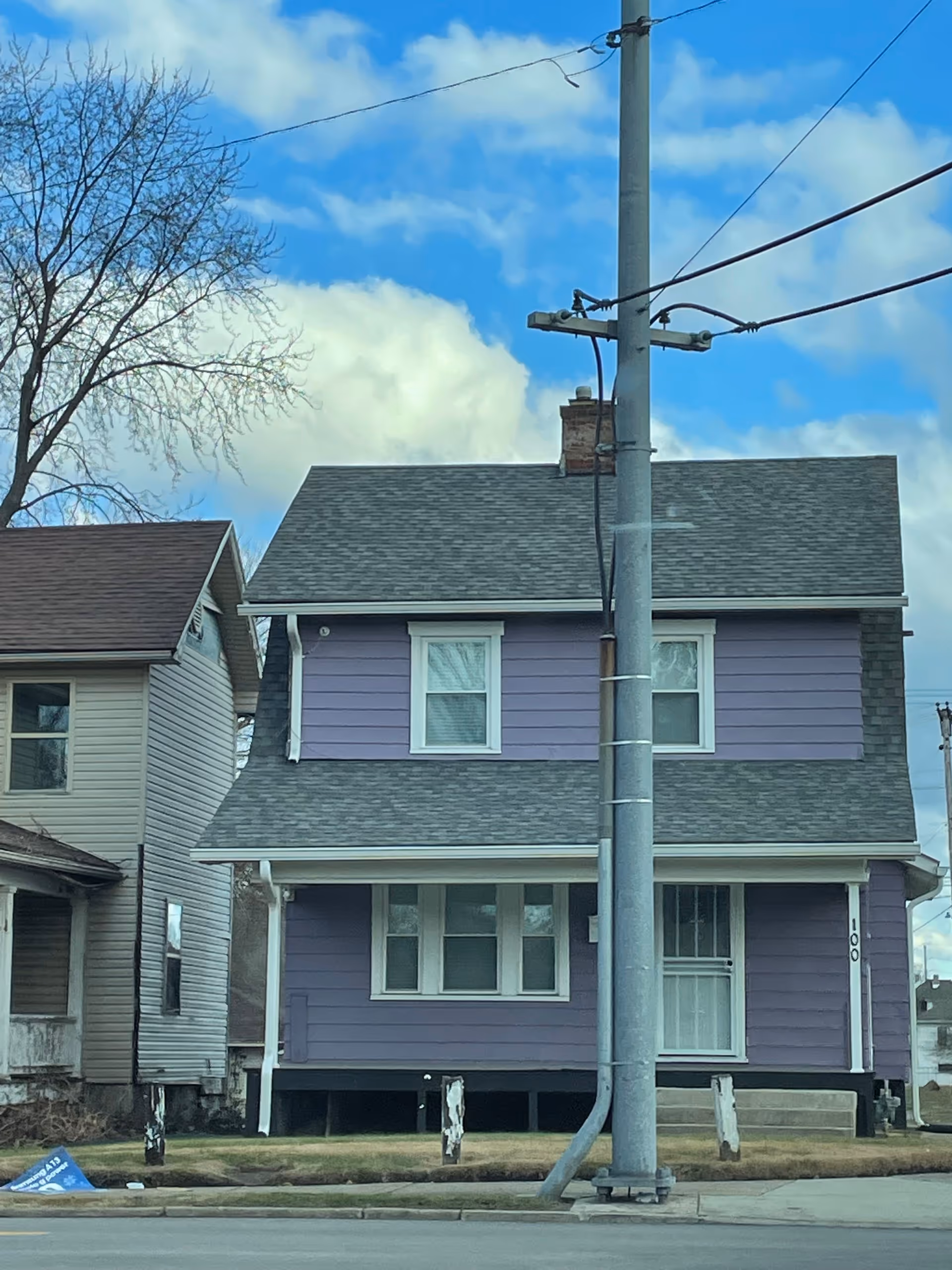 Two-story lavender house with white trim on a street, utility pole and wires in foreground.