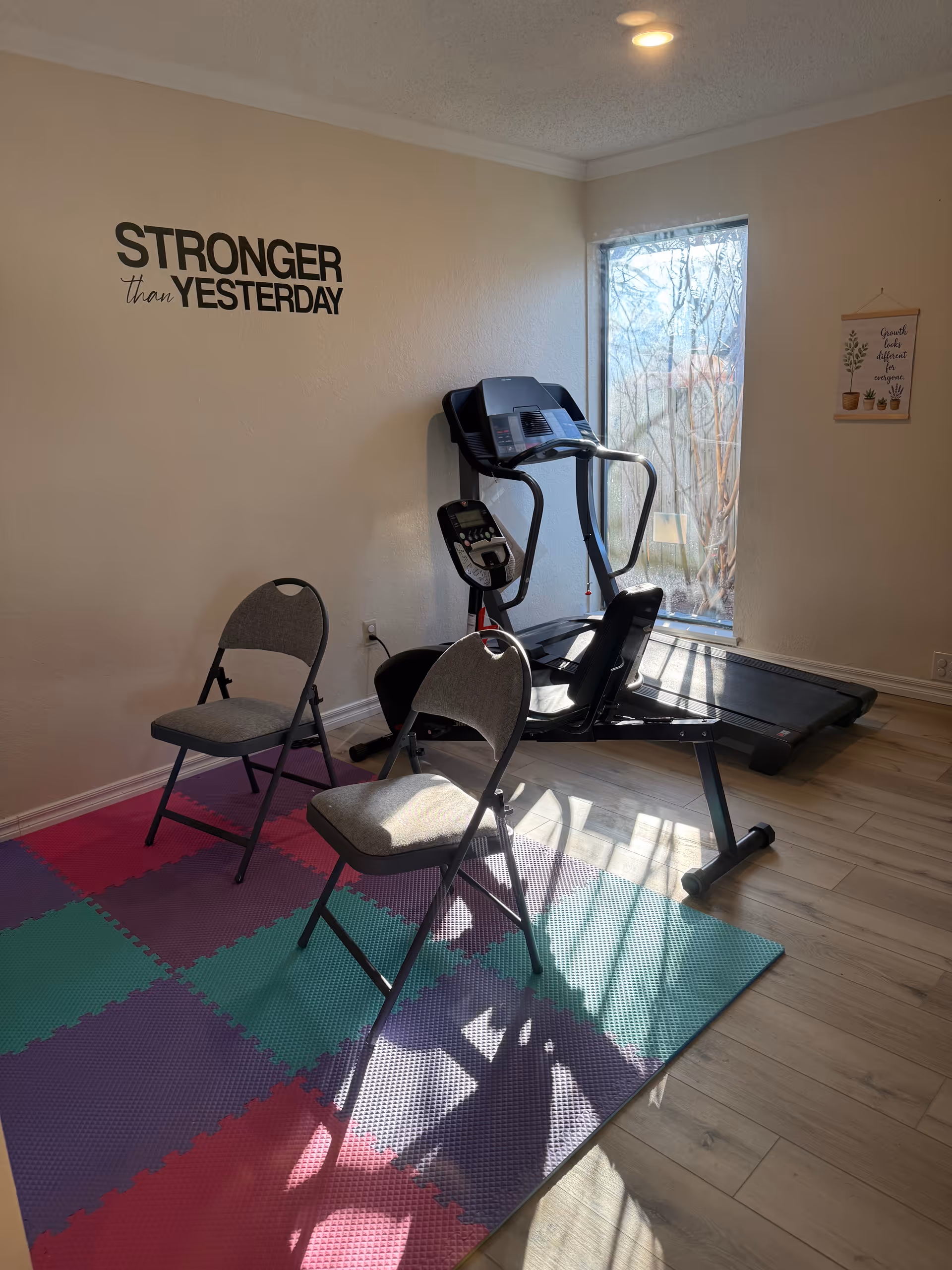 Treadmill, two chairs, and colorful mats in a small exercise nook with motivational wall art.