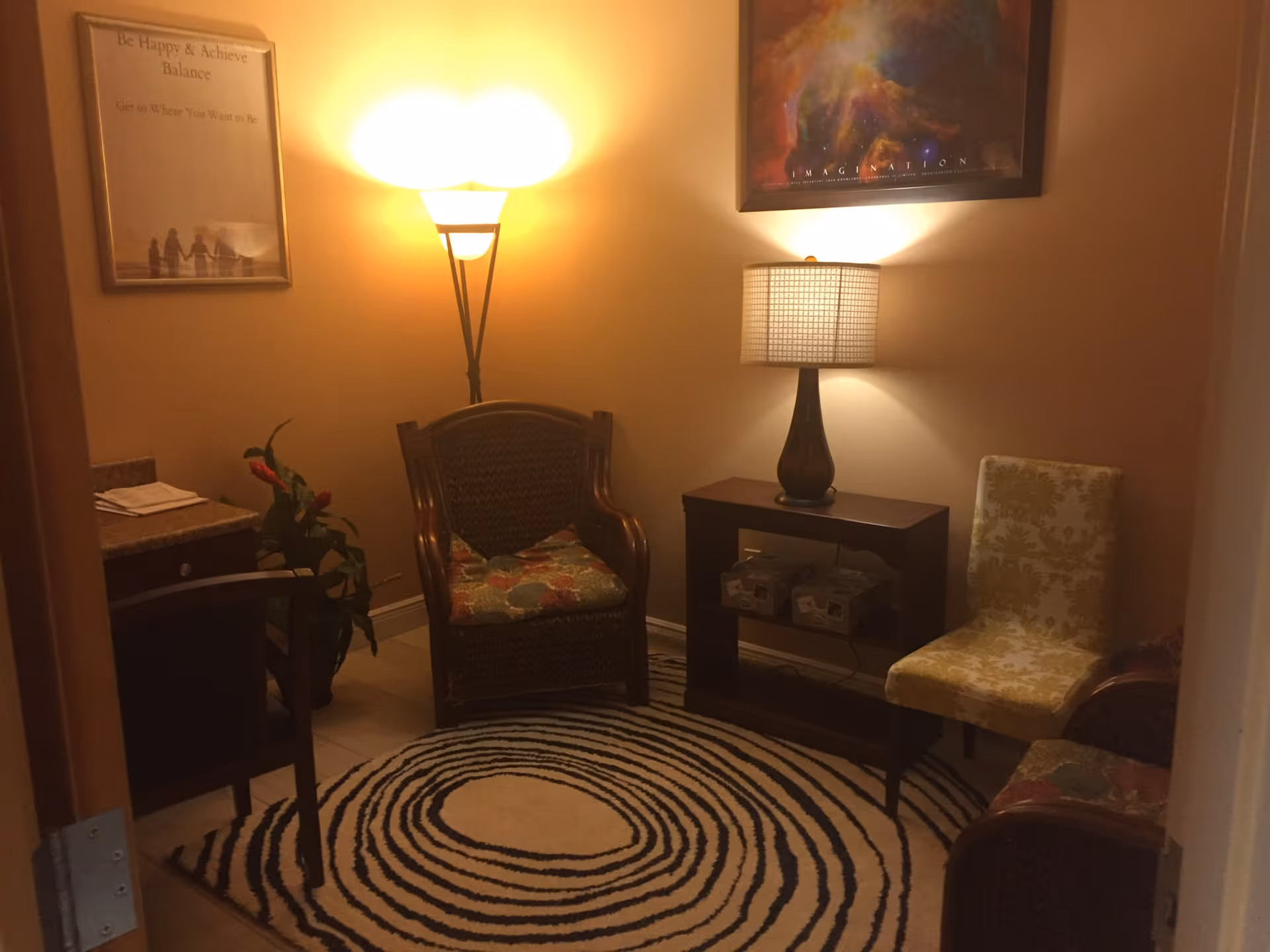 Small lounge area with wicker chair, lamp, side table, and patterned rug.