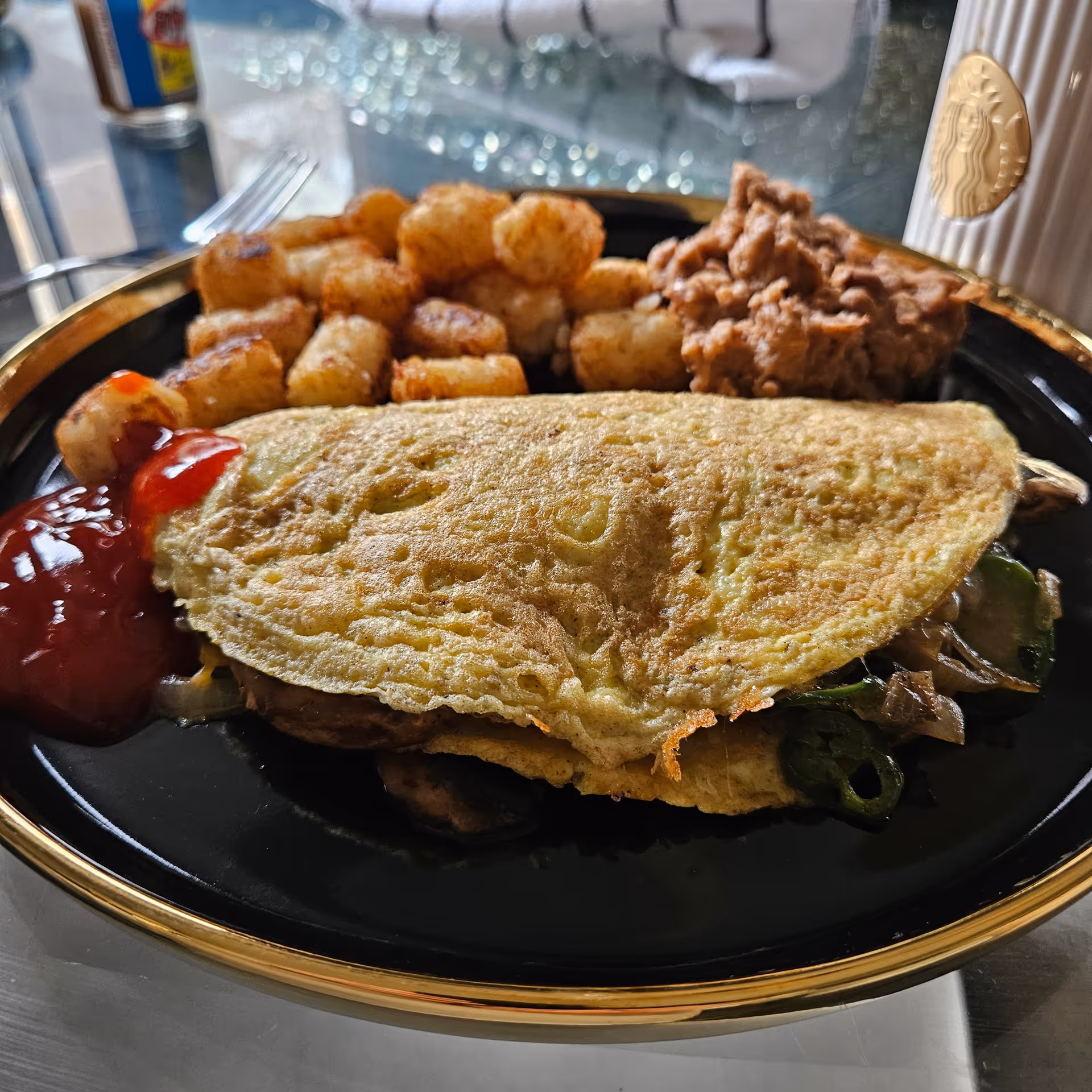 A plated meal featuring a sandwich with hash browns and ketchup on a black plate.