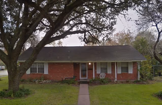 Single-story brick building with a central front door, path, lawn, and trees.