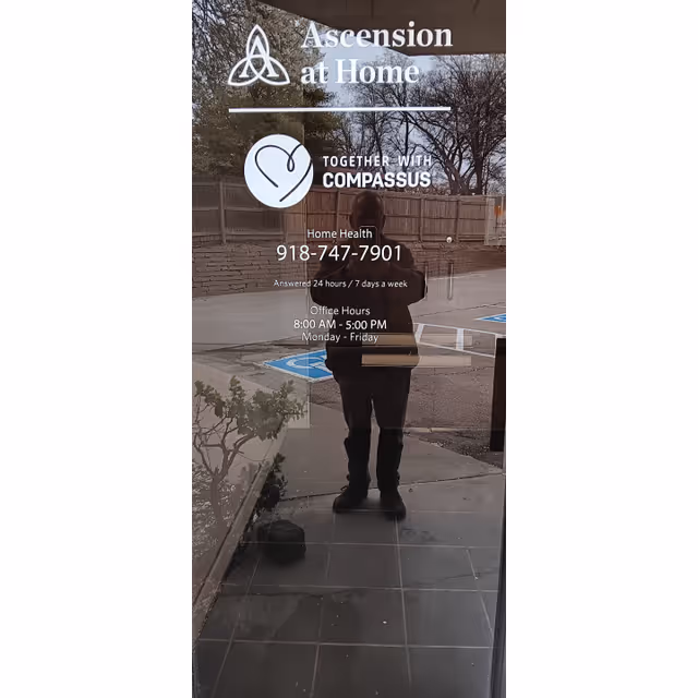 Reflection of a person in a glass door with Ascension at Home signage and contact info.