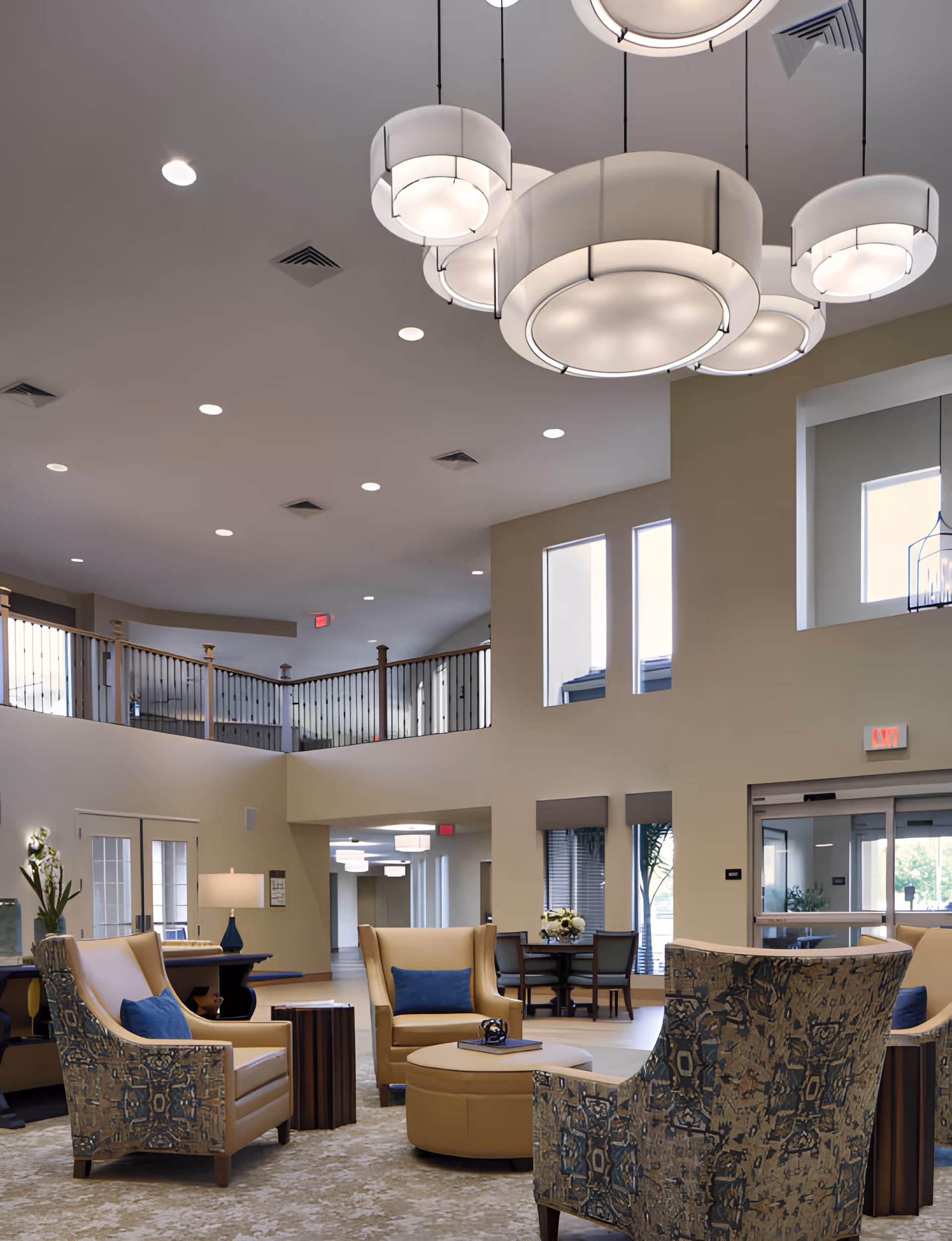 Spacious two-story lobby with modern pendant lights and a seating area of armchairs and an ottoman beneath a balcony railing.