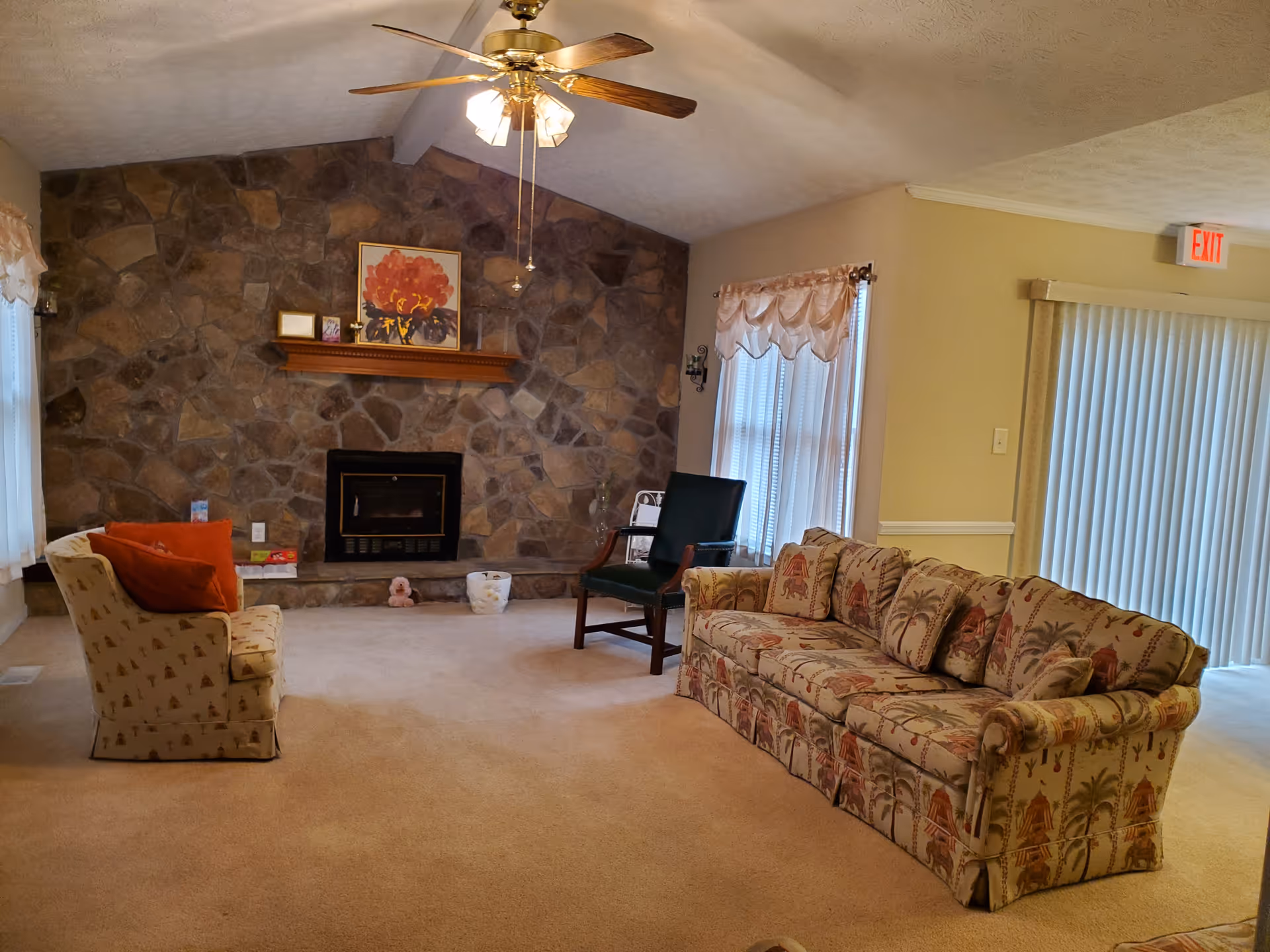 Cozy living room featuring a stone fireplace, floral sofa, and armchair.
