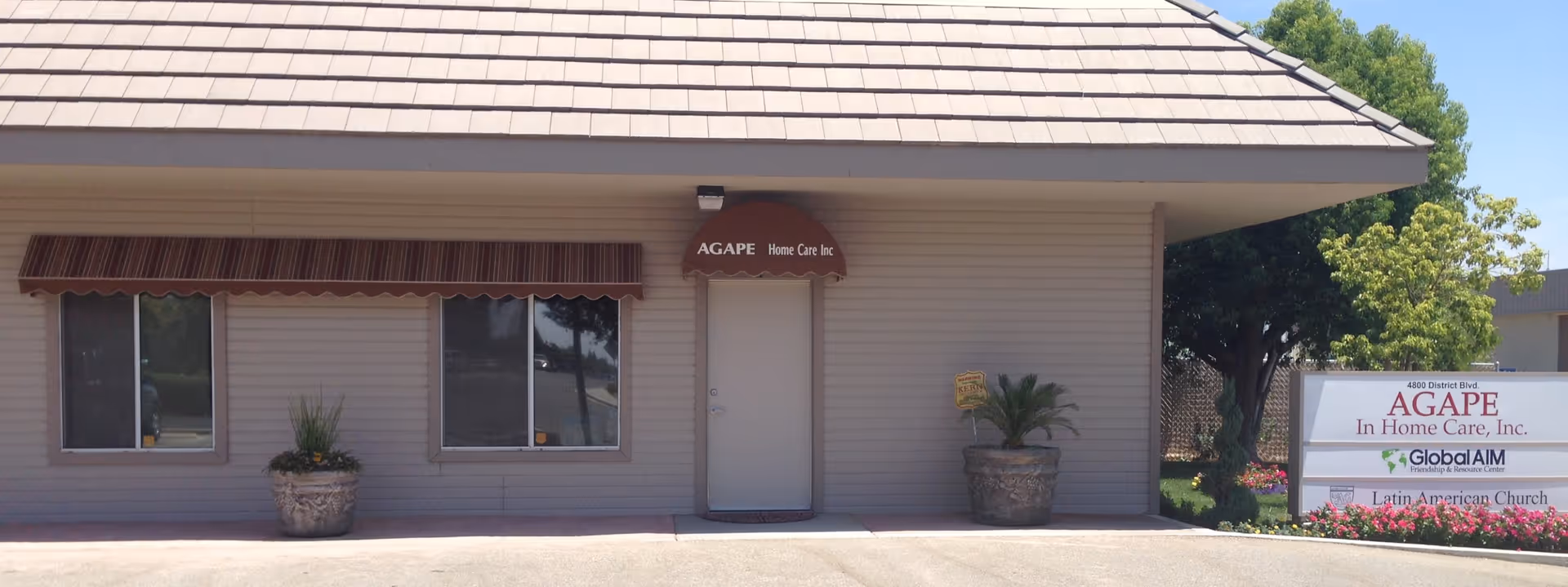 Front view of Agape In Home Care Inc building with doorway, windows, and potted plants.