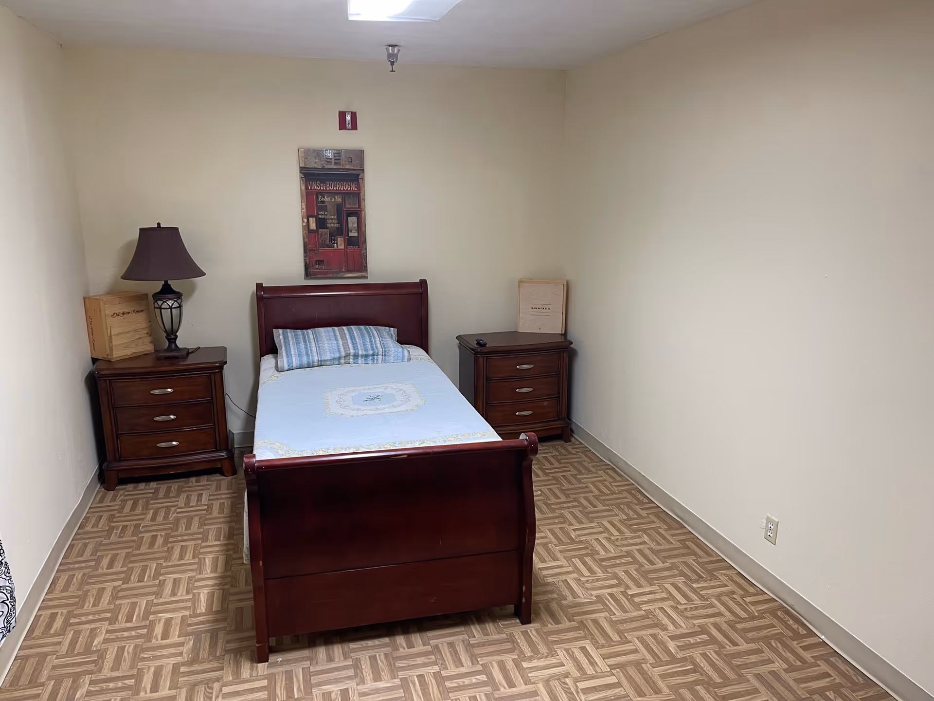 Single wooden bed with blue bedding, flanked by nightstands in a small bedroom
