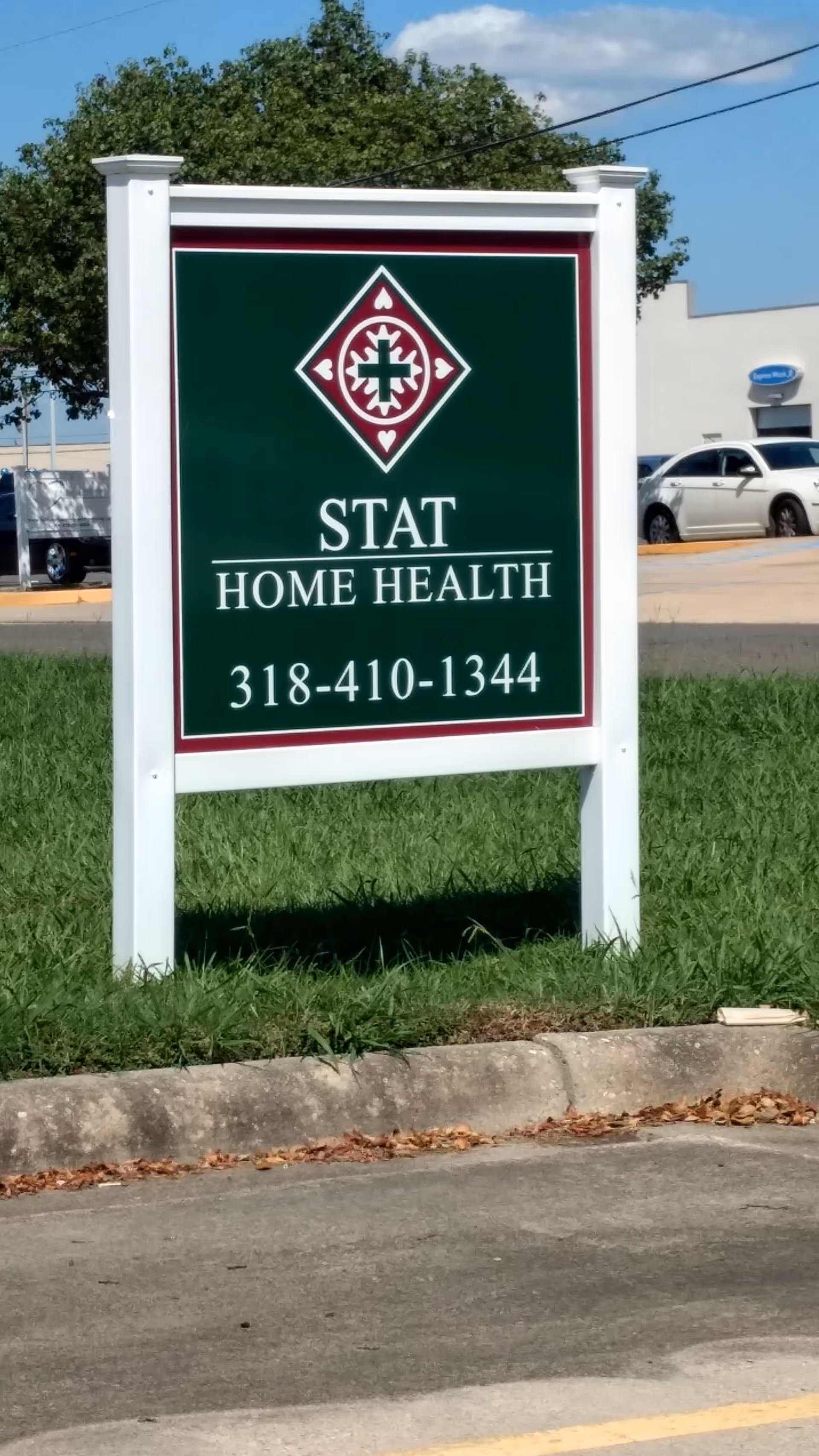 Green STAT HOME HEALTH sign on two white posts beside a grassy area.