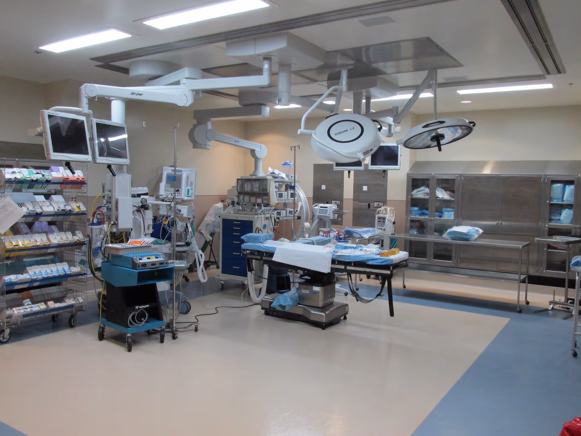 Modern operating room with surgical table, overhead lights, and medical equipment.