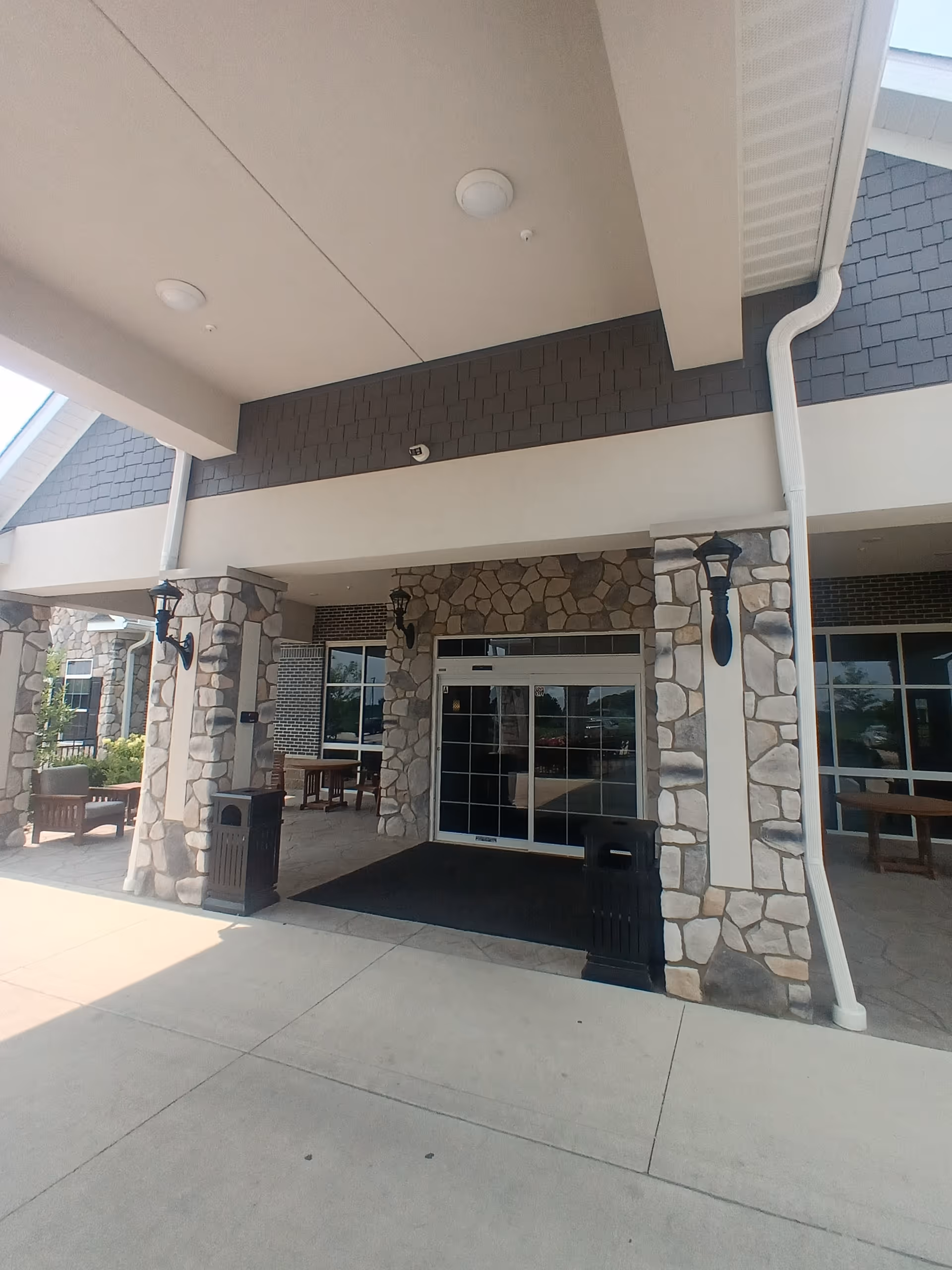 Stone building front entrance with columns, glass doors, and a covered walkway