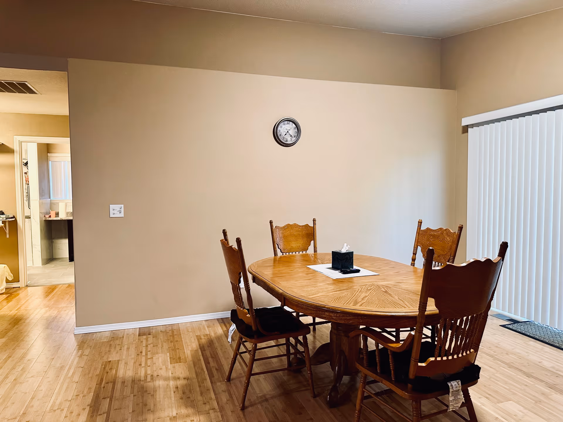 Round wooden dining table with six chairs in a beige, well lit dining room.