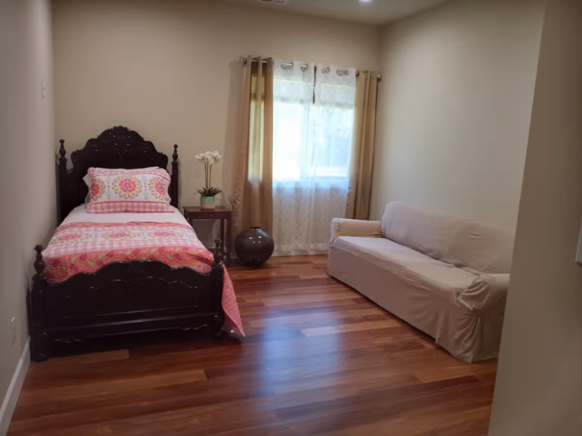 A cozy bedroom with a dark carved bed, pink bedding, and a beige sofa.