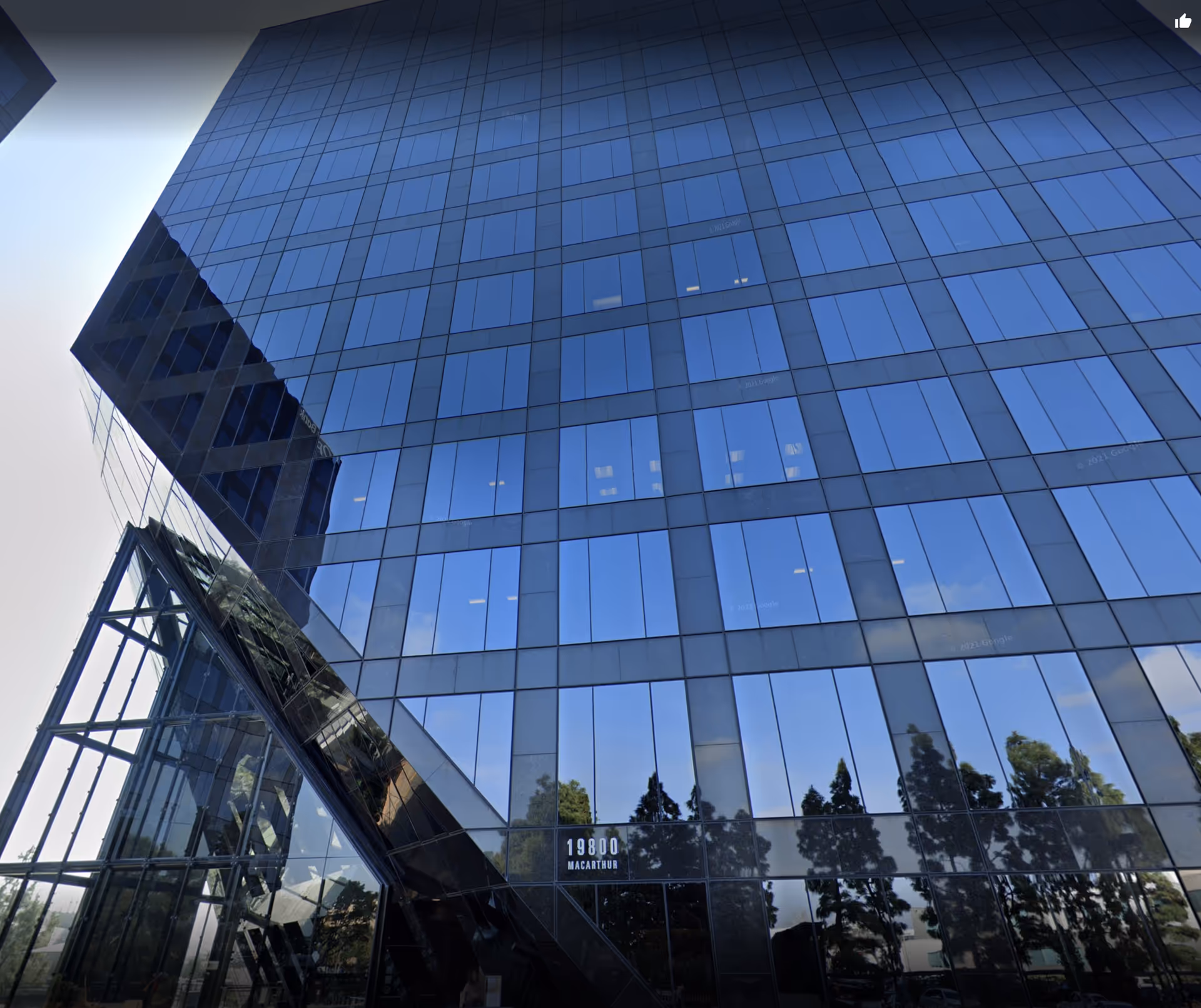 Modern glass building exterior with angular entrance and reflected trees.