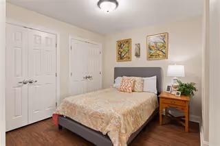 Cozy bedroom with bed, nightstand, lamp, closet doors, and framed art.