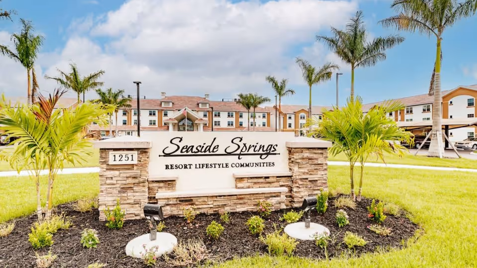 Seaside Springs Retirement Community entrance sign with landscaped lawn palm trees and the building in background.