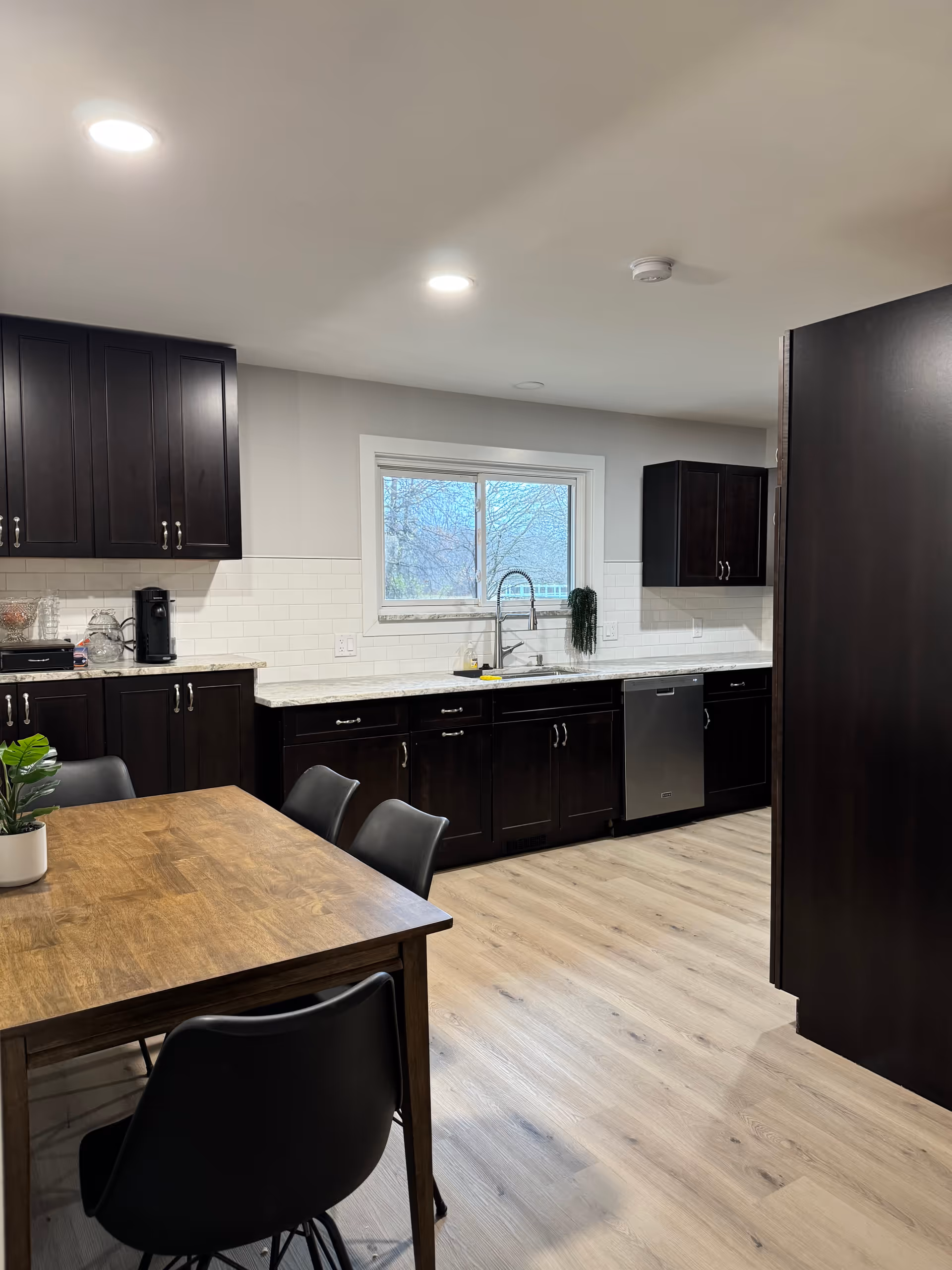 Dark wood cabinets line a bright kitchen with a wooden dining table and stainless steel appliances.
