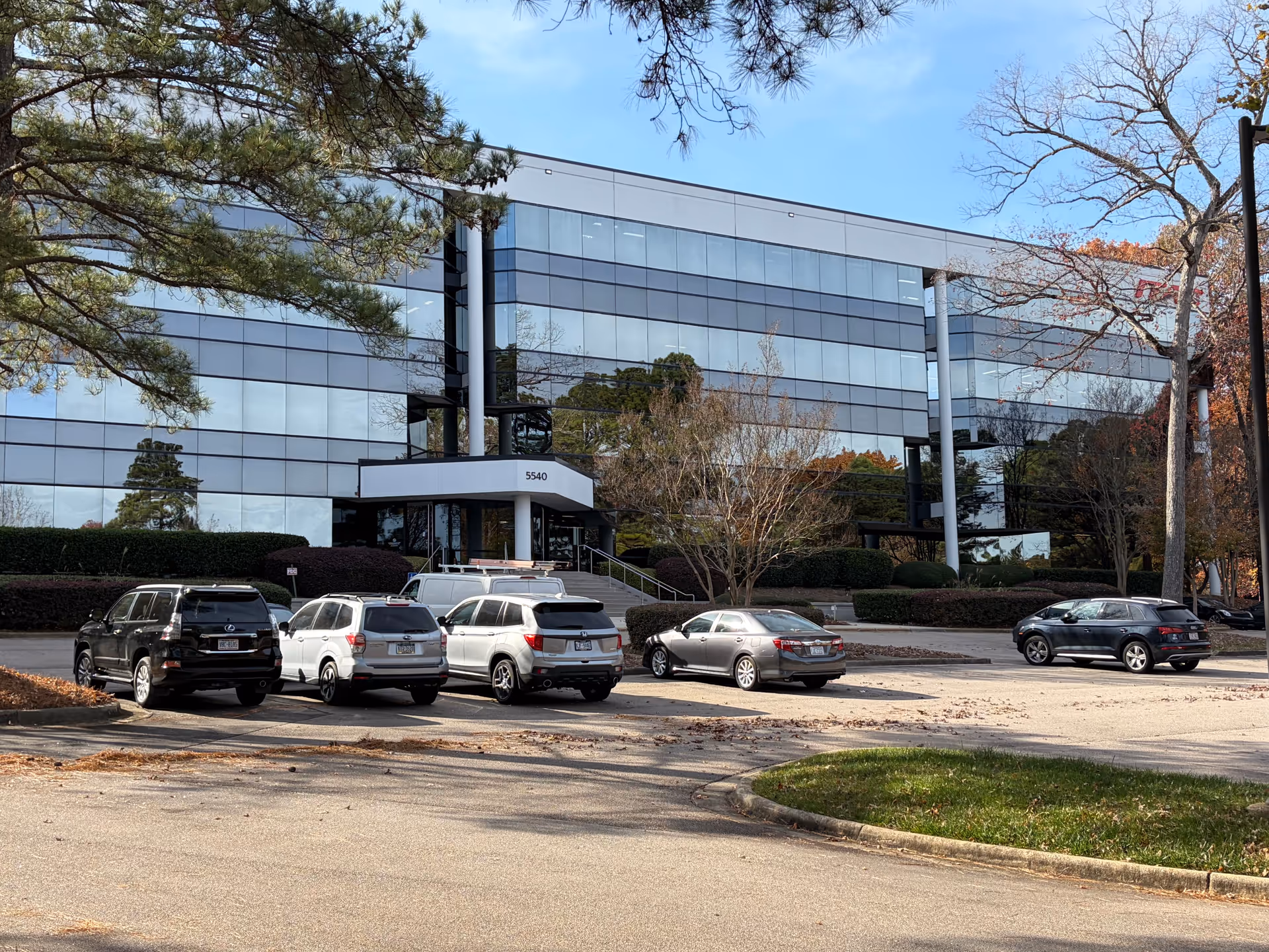 A modern glass-front office building with a parking lot in front.
