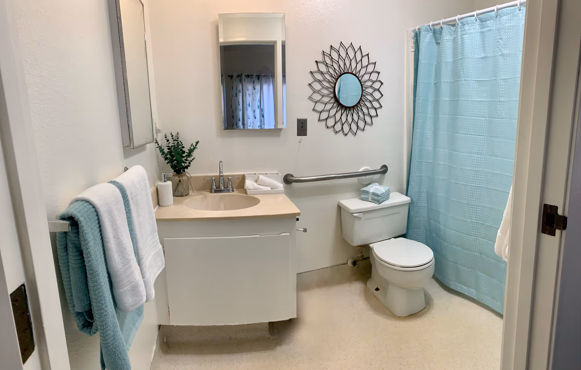 Clean bathroom featuring a sink, toilet, grab bar, and blue shower curtain.