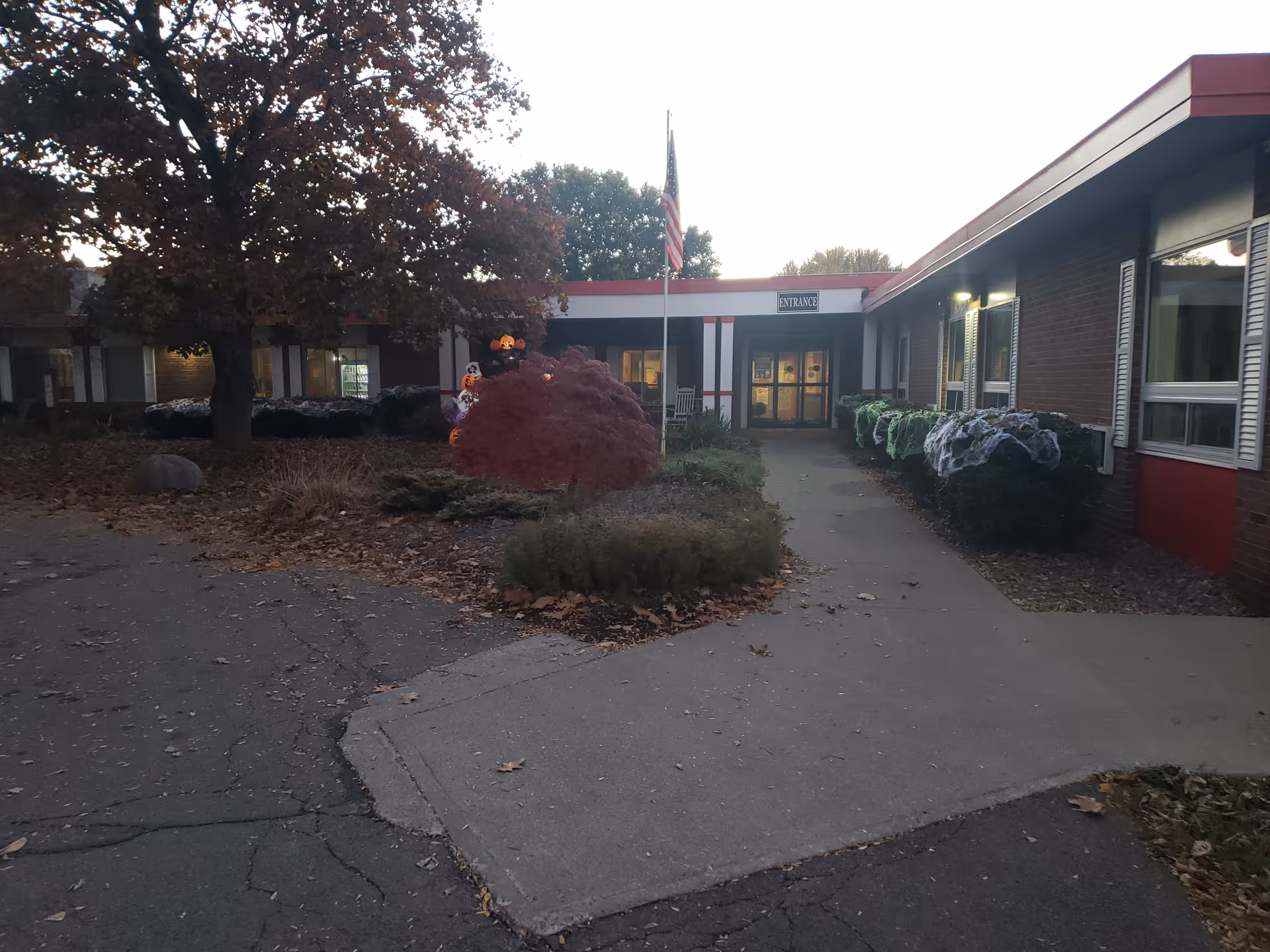 Exterior view of Cortland Park Rehabilitation and Nursing Center with entrance, flag, and autumn landscaping.