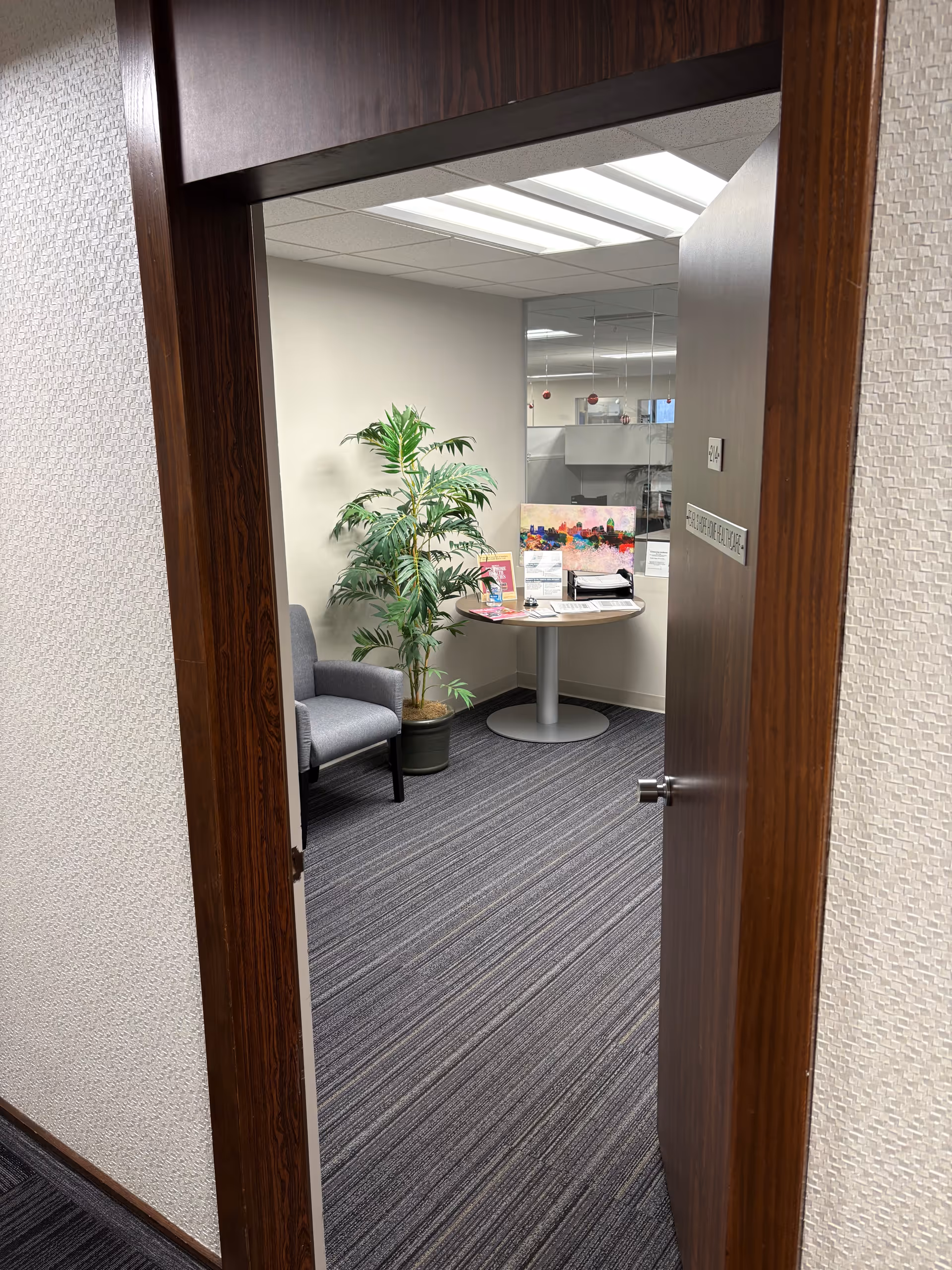 Open doorway reveals a small office lounge with chairs, round table, and plant.