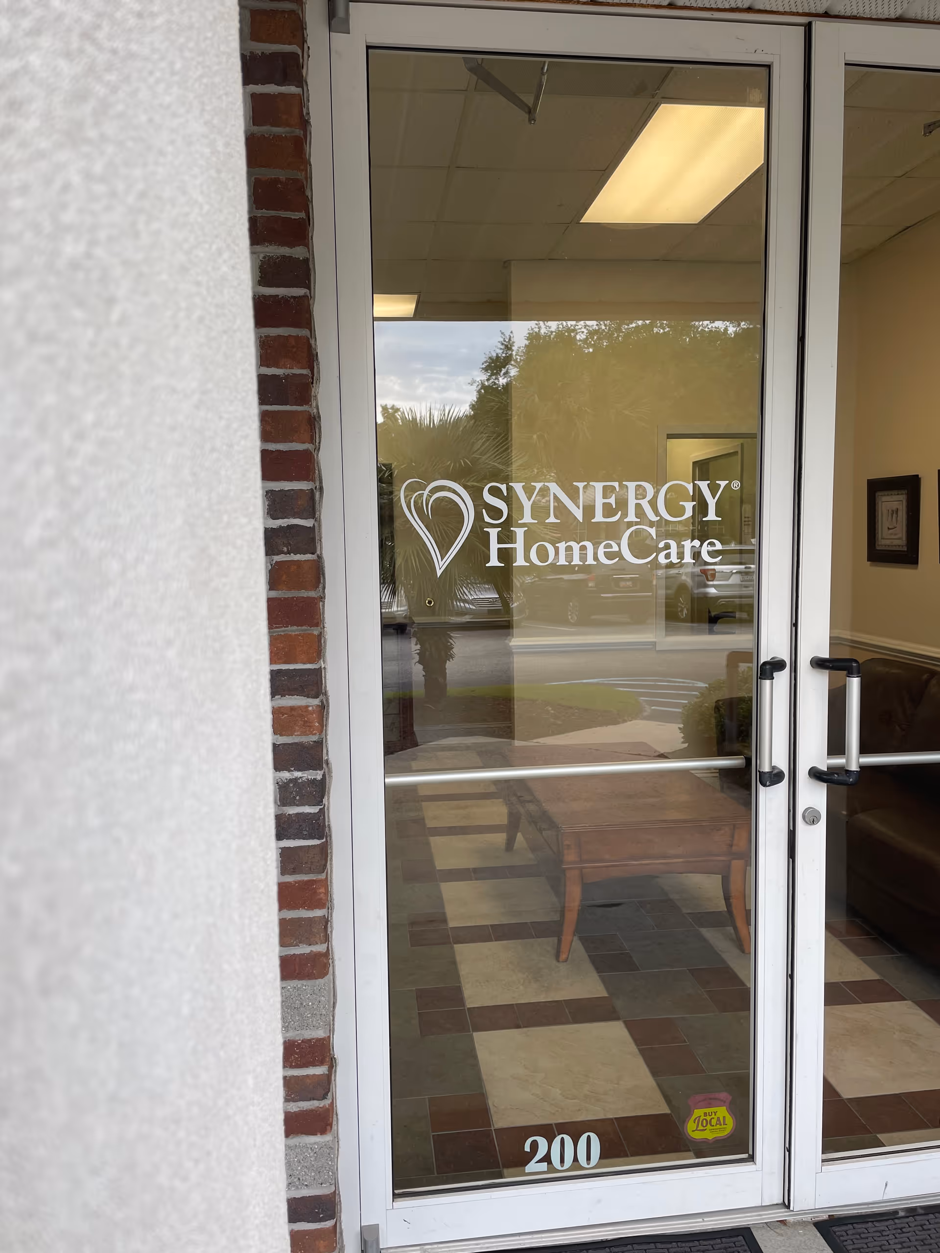 Glass entrance door with Synergy HomeCare logo; lobby seating visible inside.