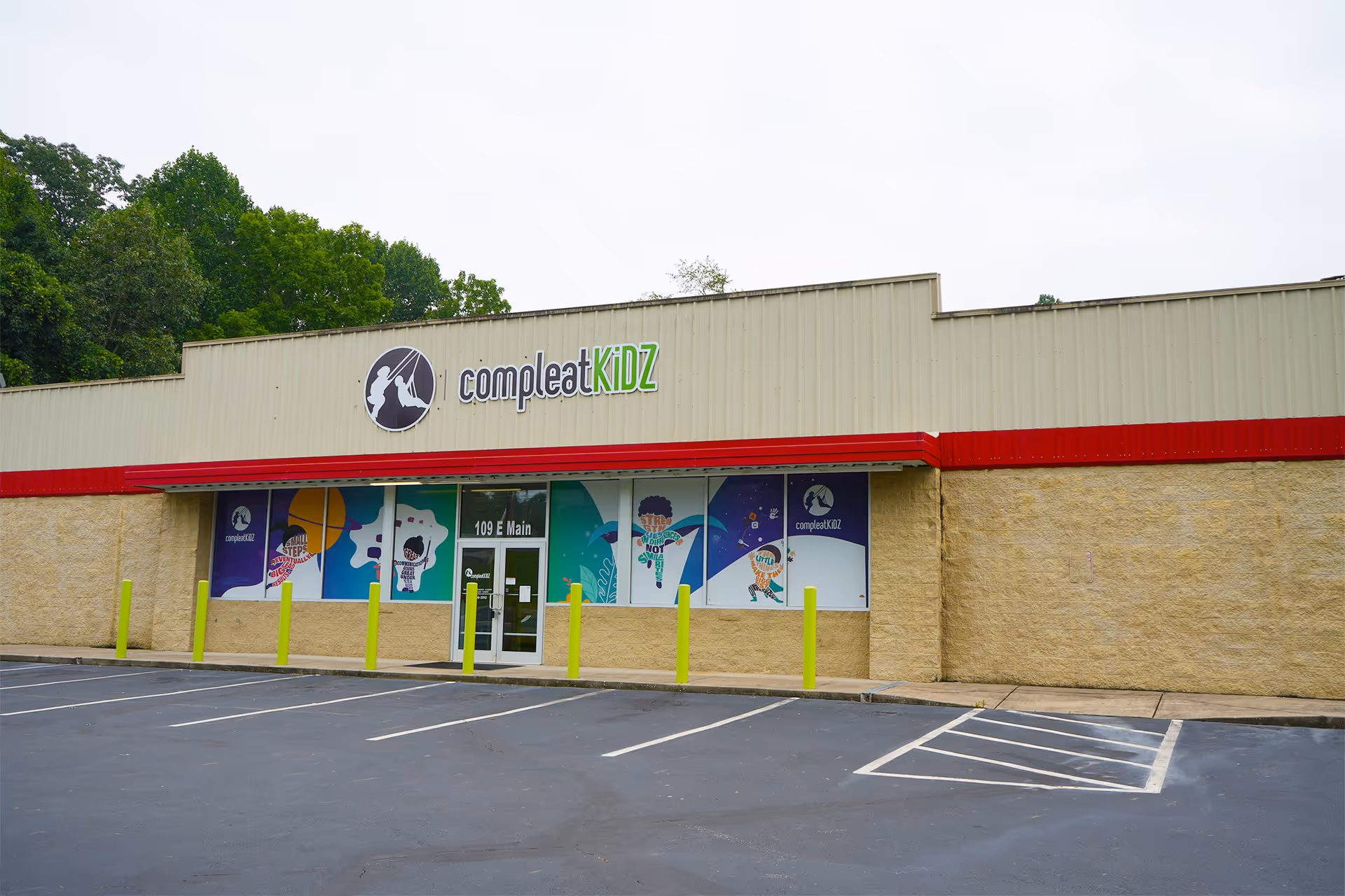 Beige storefront with Compleat Kidz sign and colorful windows, empty parking lot in front