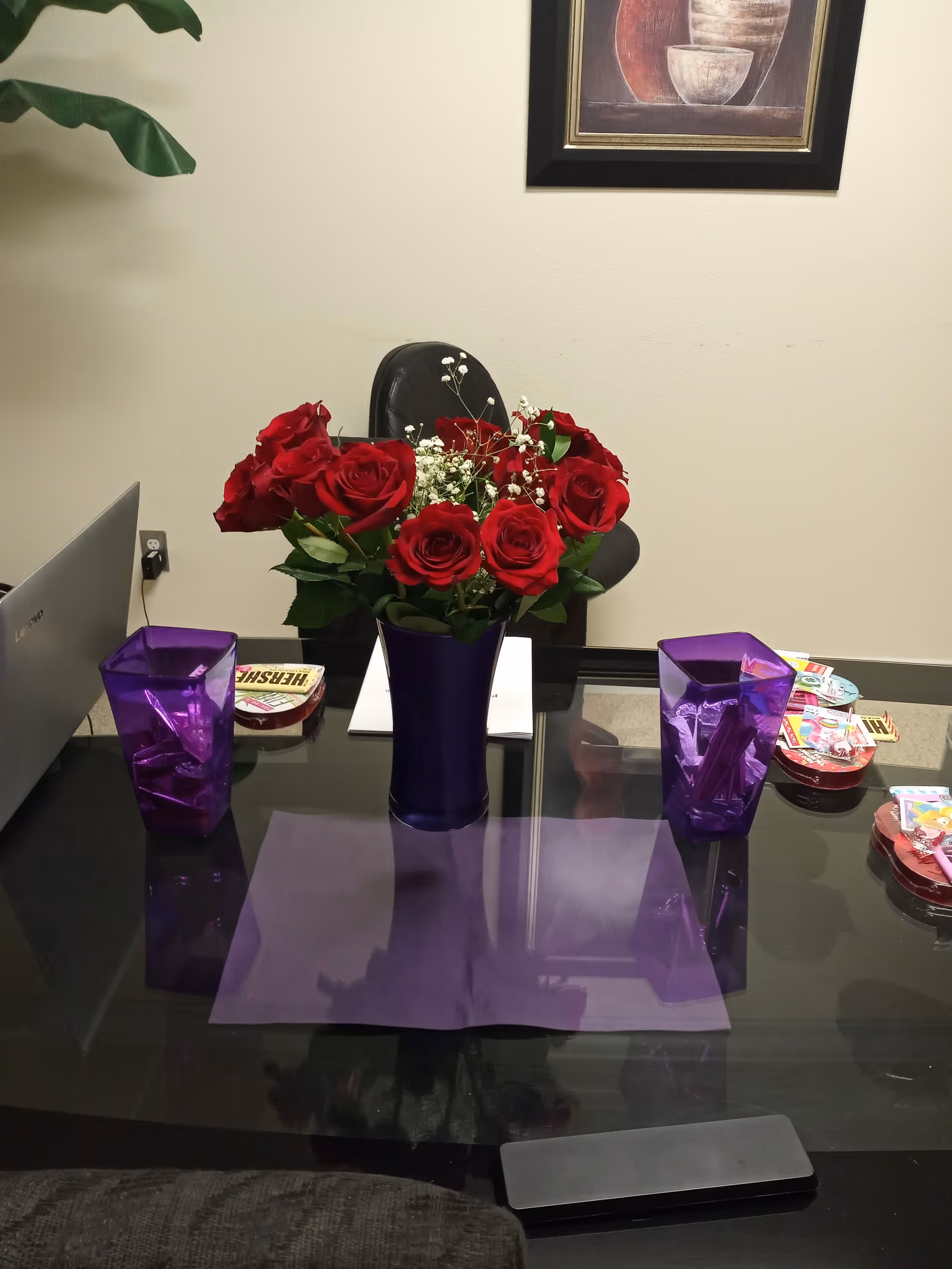Office desk with a purple vase of red roses and assorted items.