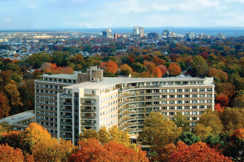 An aerial view of a large senior living facility surrounded by autumn trees.