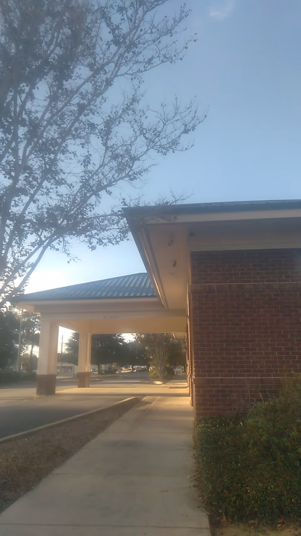 Exterior view of a brick facility with a covered walkway and a nearby tree lined sidewalk.