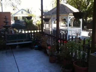Outdoor porch with railing, bench, potted plants, and white gazebo in background.