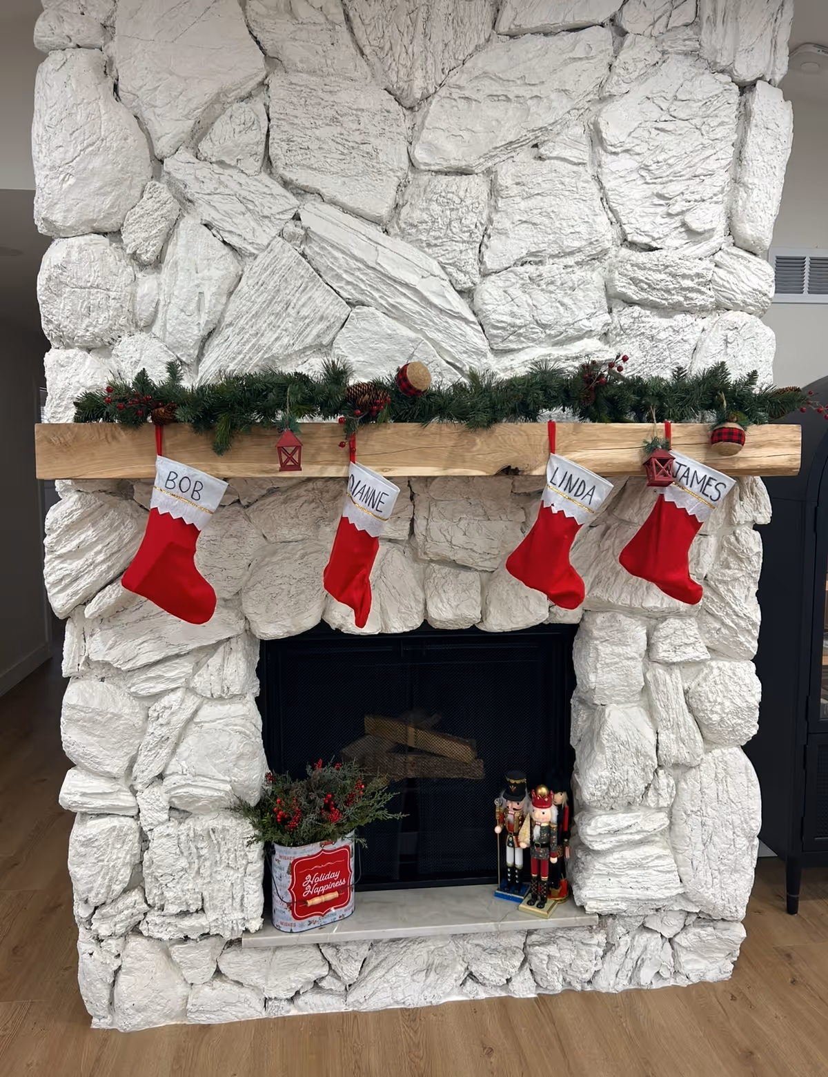 White stone fireplace adorned with garland and four named Christmas stockings near Nutcrackers.