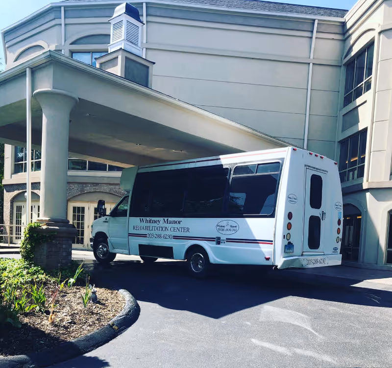 Whitney Manor Rehabilitation Center shuttle bus parked at the exterior entrance.