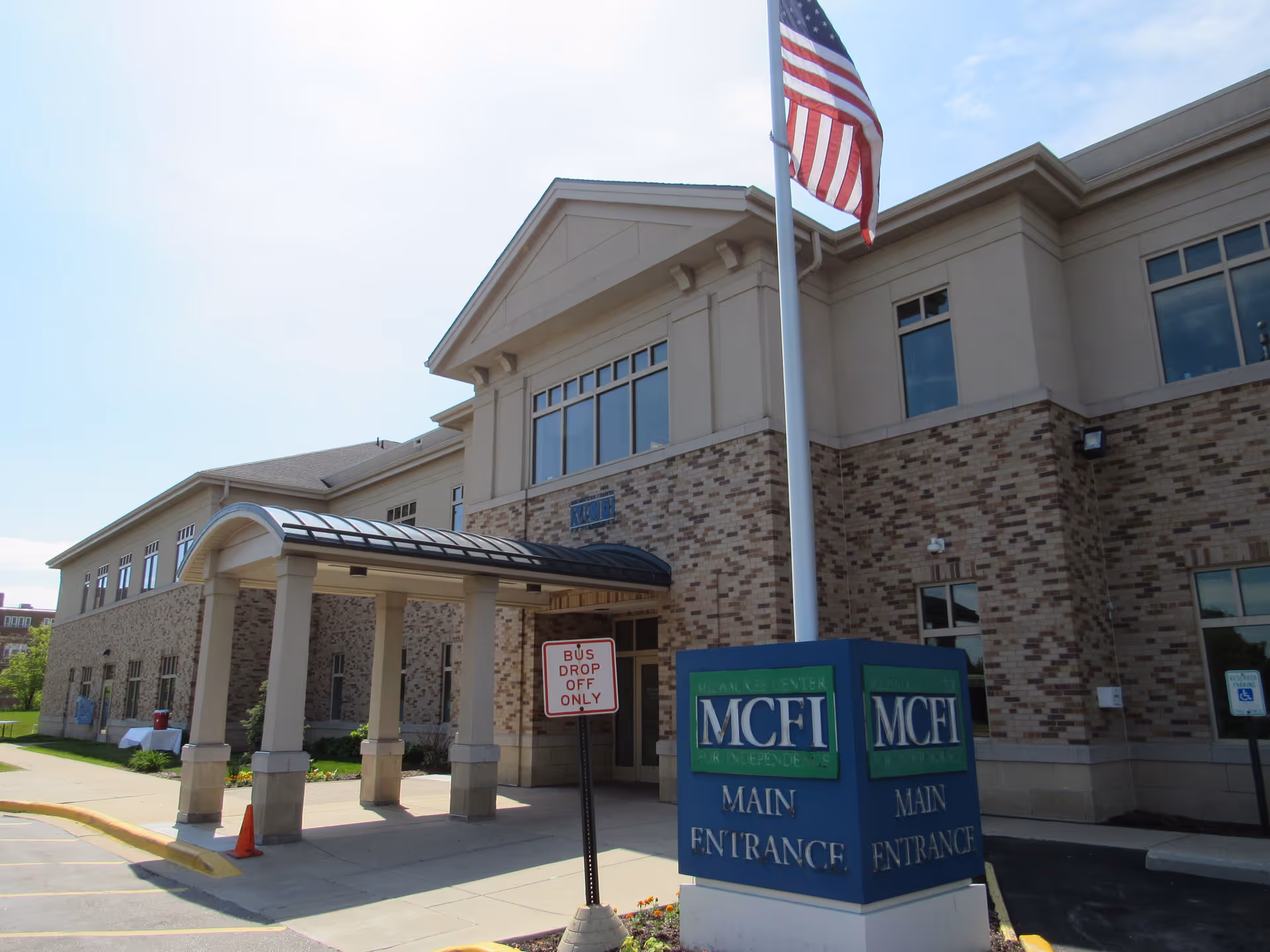 Exterior view of a senior living facility entrance with canopy, brick facade, and American flag.