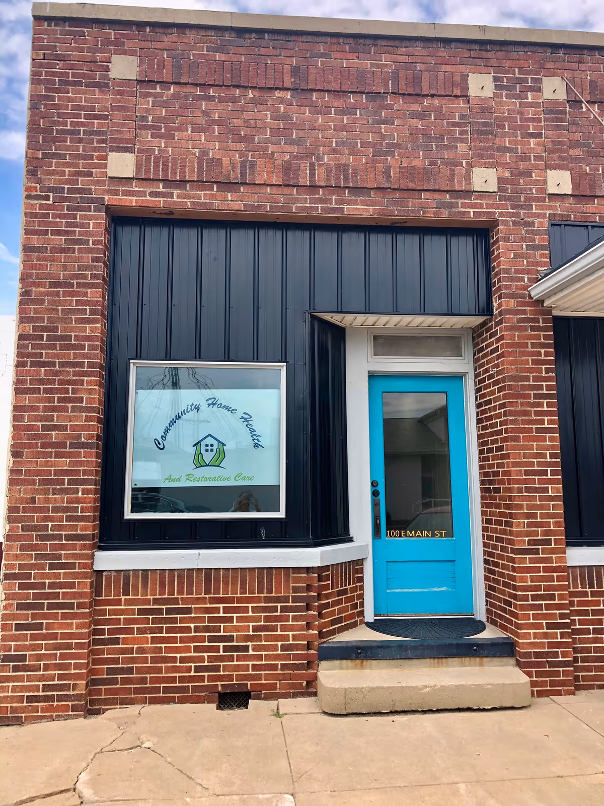 Brick building exterior with teal door and window sign for Community Home Health and Restorative Care