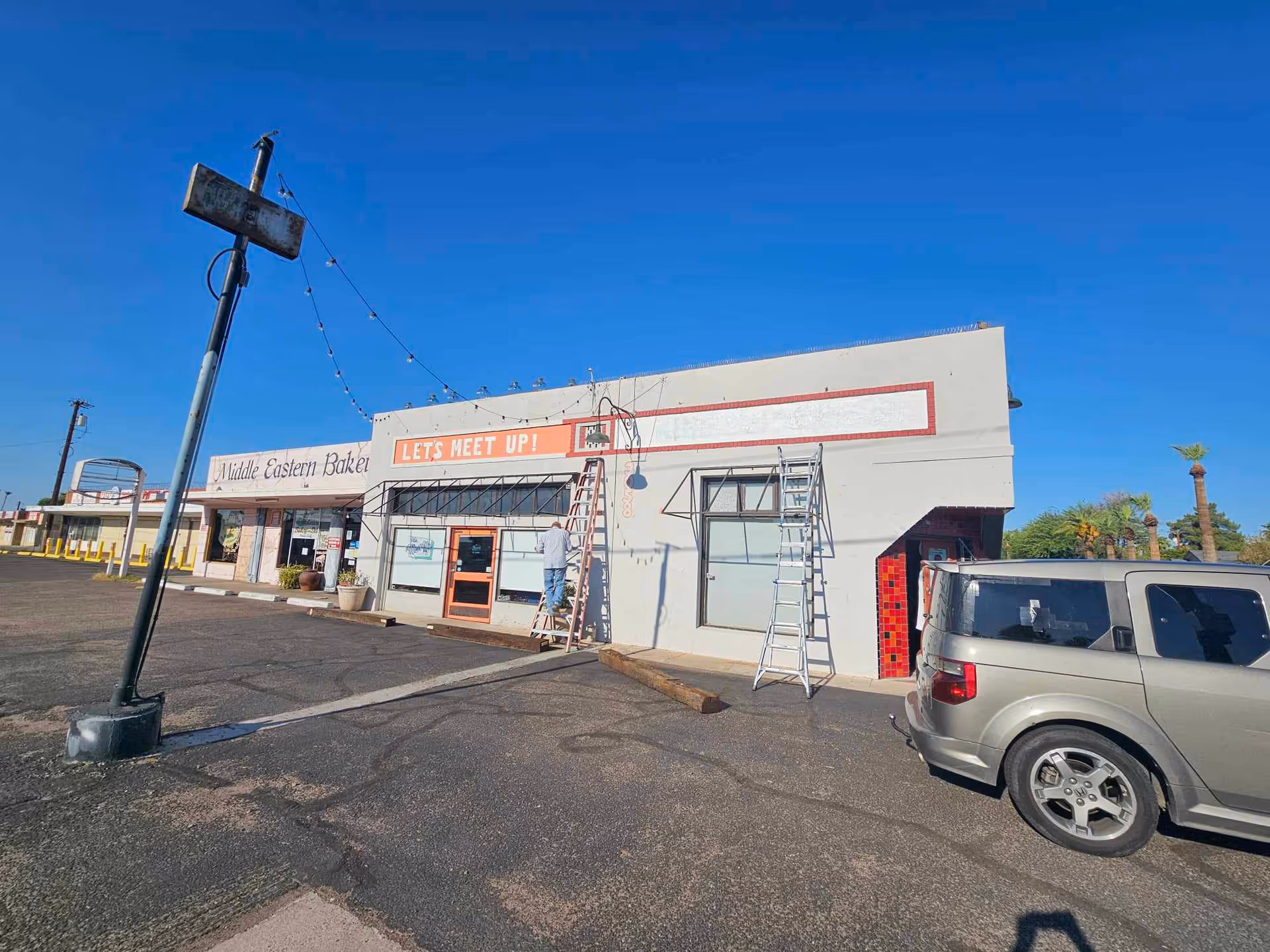 Exterior view of a storefront building with a bakery, ladders, and a parked SUV.