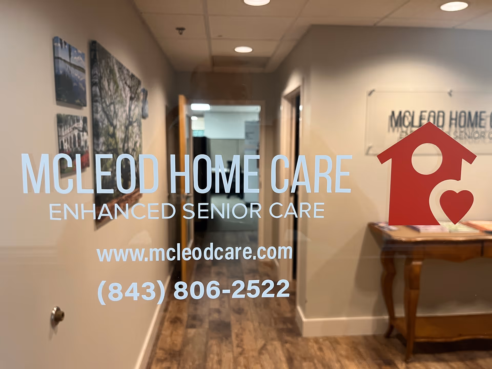 Glass wall shows McLeod Home Care logo and contact details in an interior hallway.
